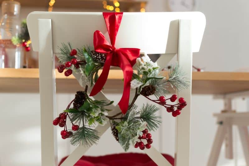 cozy-decorated-with-christmas-decorations-with-red-ribbon-and-fir-branches-white-kitchen-chair-130806386-min